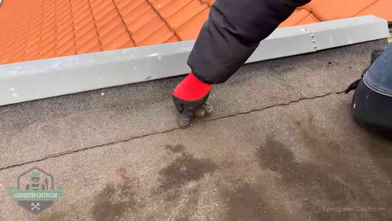 Vakman wijst een naad met vochtplekken aan op een bitumen plat dak in Castricum