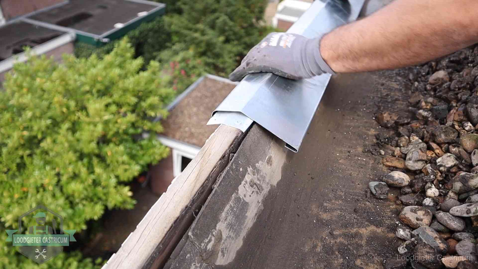 Dakdekker plaatst een zinken deklijst op een dakrand met uitzicht over een woonwijk in Castricum