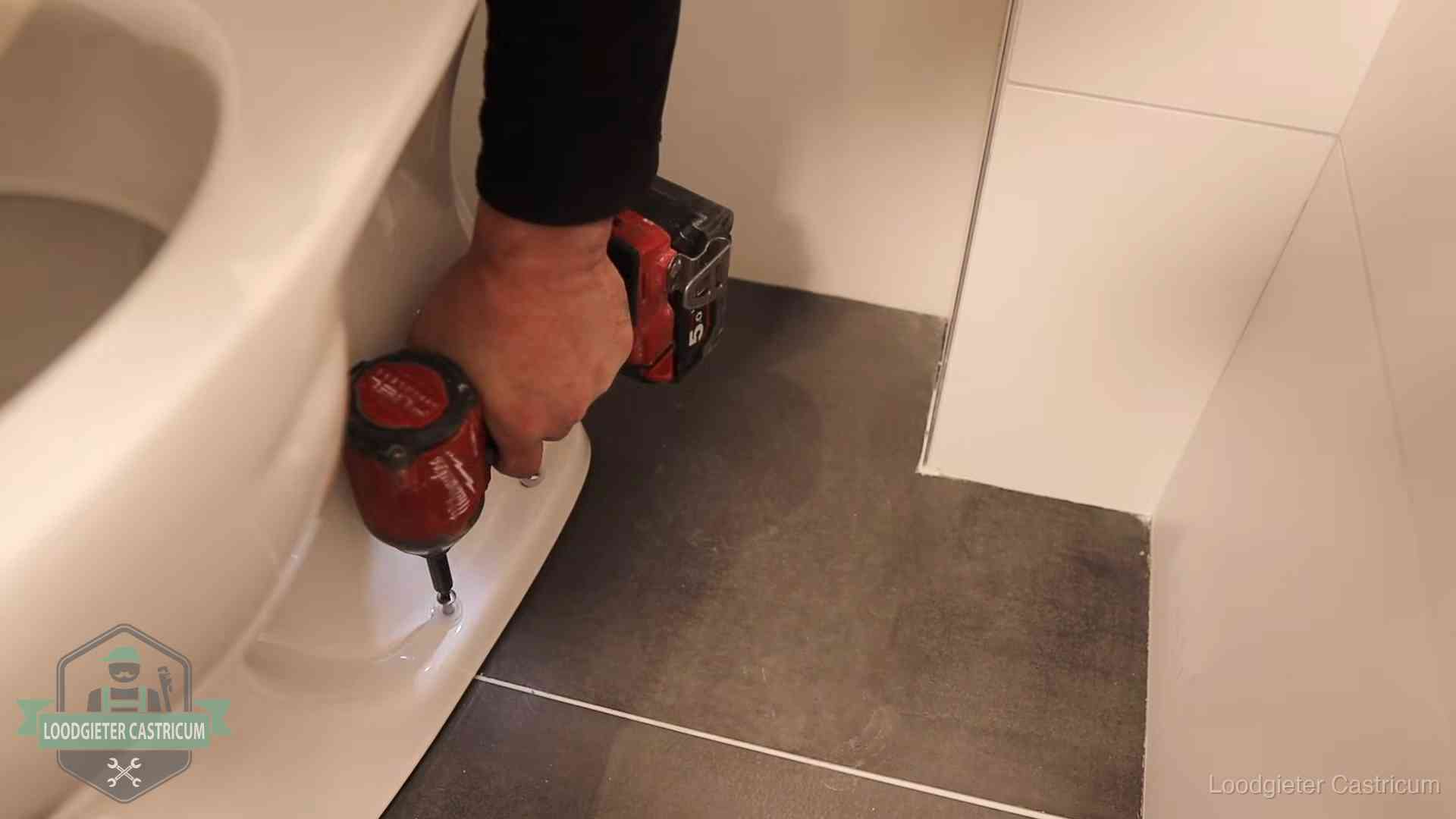Loodgieter zet de voet van een wc-pot vast op de tegelvloer in Castricum